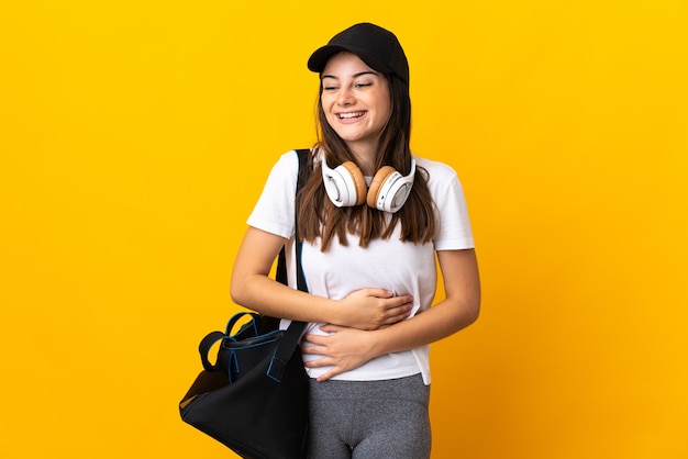 Junge Sportfrau mit Sporttasche lokalisiert auf gelber Wand, die viel lächelt