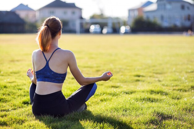 Junge sportive Frau in Yogaposition meditiert auf dem Gebiet bei Sonnenaufgang.