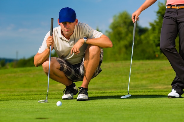 Junge sportive Paare, die Golf auf einem Kurs spielen