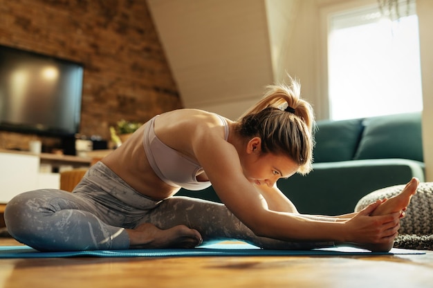 Junge Sportlerin dehnt sich beim Aufwärmen vor dem Sporttraining zu Hause