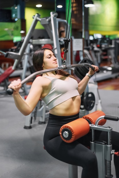 Junge Sportlerin, die auf lat Maschine im Fitnessstudio ausübt.