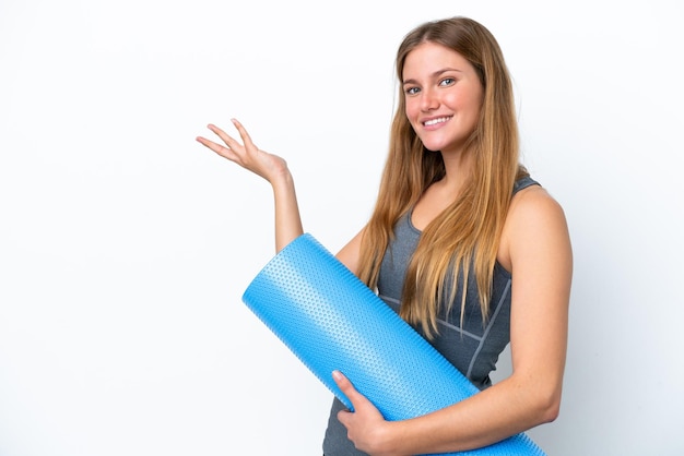 Junge Sportlerin, die zu Yoga-Kursen geht, während sie eine Matte hält, die die Hände zur Seite streckt, um zum Kommen einzuladen