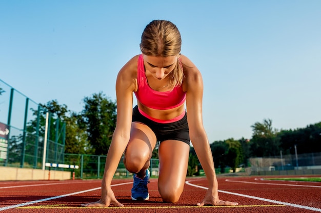 Junge Sportlerin in Startposition bereit, ein Rennen auf der Rennstrecke zu starten