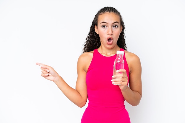 Junge Sportlerin mit einer Flasche Wasser isoliert auf weißer überraschter und zeigender Seite