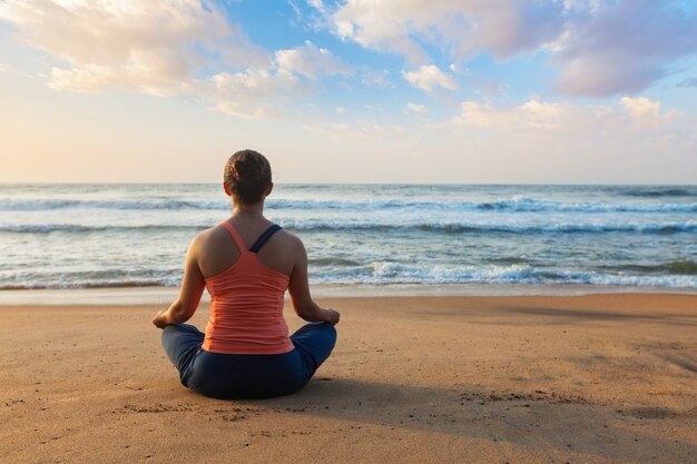 Junge sportliche fit Frau, die Yoga draußen am Strand tut