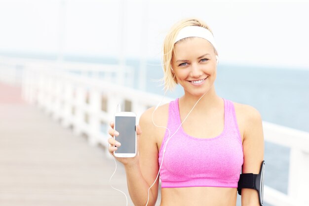 Junge sportliche Frau am Pier über dem Meer mit Telefon