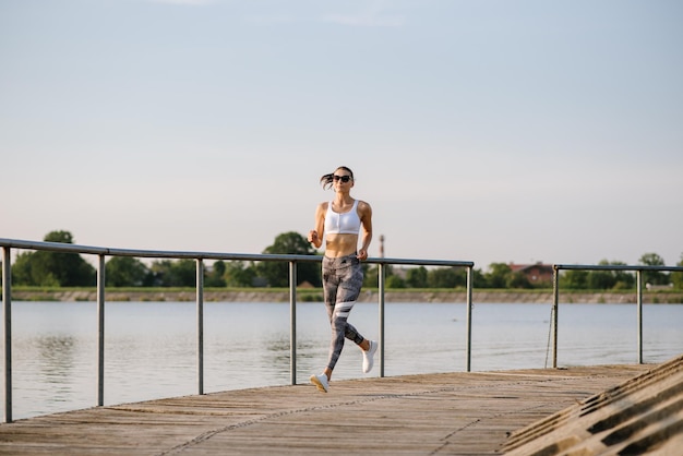 Junge sportliche Frau, die an einem warmen Sommertag im Park am Teich läuft