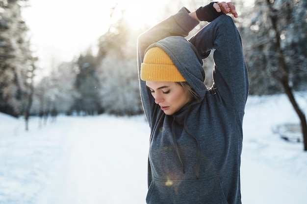 Junge sportliche Frau, die sich an sonnigen und verschneiten Tagen vor ihrem Wintertraining aufwärmt