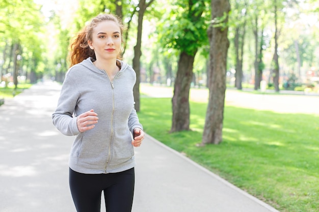 Junge sportliche Frau, die während des morgendlichen Trainings im grünen Park läuft, Kopienraum