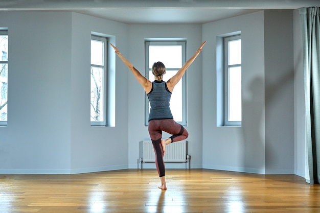 Junge sportliche Frau, die Yoga praktiziert, trainiert, Sportbekleidung, Hosen und Top trägt, Innennahaufnahme, Yoga-Studio