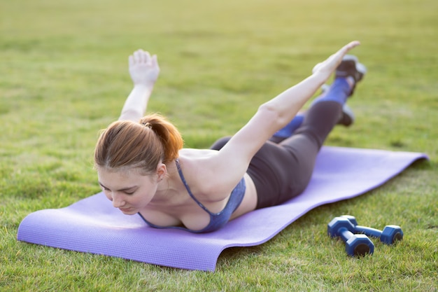 Junge sportliche frau im sportkleidungstraining im feld bei sonnenaufgang. mädchen, das in der plankenposition auf gras in einem stadtpark steht.