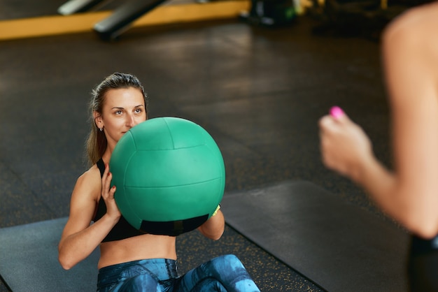 Junge sportliche Frau in Sportbekleidung, die Bauchmuskelübungen mit Fitnessball im Fitnessstudio mit macht