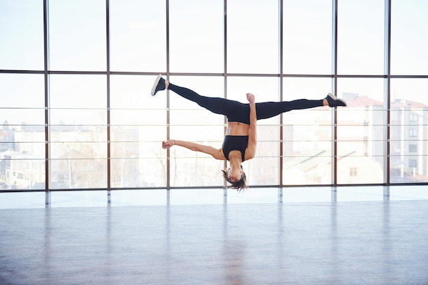 Junge sportliche Frau in Sportkleidung springt und macht athletische Tricks gegen Fenster in der Luft.