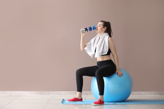 Junge sportliche Frau mit fitball und Flasche Wasser nahe Farbwand