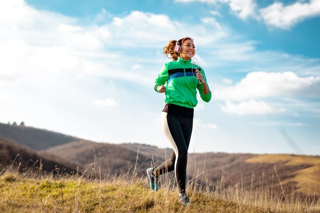 Junge sportliche Frau mit Kopfhörern beim Joggen in der Natur.