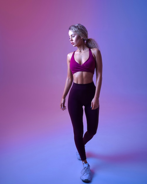 Junge sportliche Frau mit perfektem Körper posiert im Studio, Neonhintergrund. Sportlerin beim Fotoshooting, Sportkonzept, aktive Lifestyle-Motivation