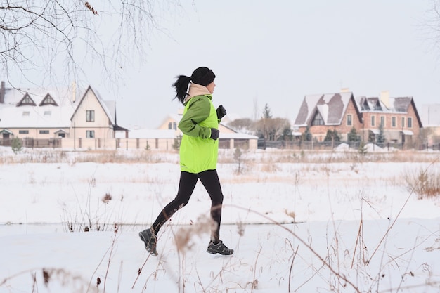 Junge sportliche Frau mit Pferdeschwanz, der nahe an den Landhäusern während des Trainings im Winter läuft