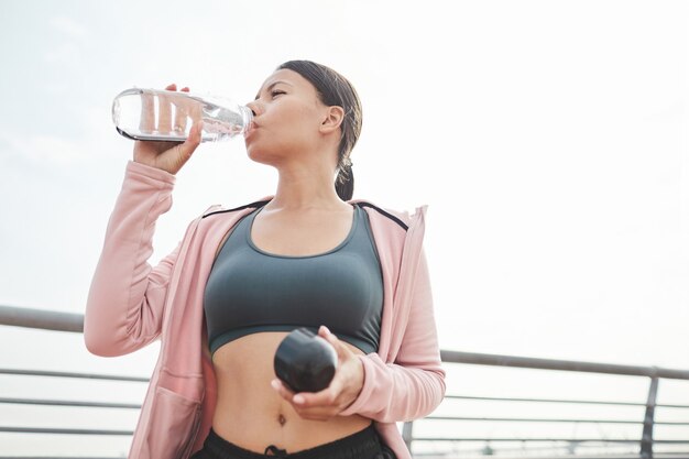 Junge sportliche Frau trinkt Wasser aus der Flasche nach dem Sporttraining im Freien