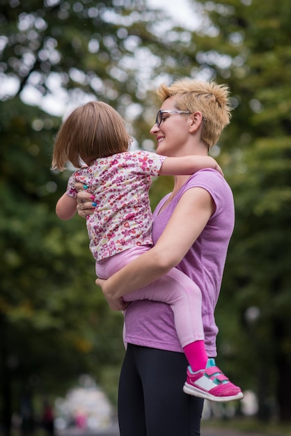 junge sportliche mutter trägt kleine tochter in den armen beim joggen in einem stadtpark, outdoor-sport und fitness