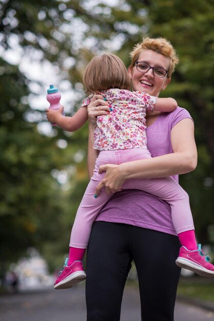 junge sportliche mutter trägt kleine tochter in den armen beim joggen in einem stadtpark, outdoor-sport und fitness