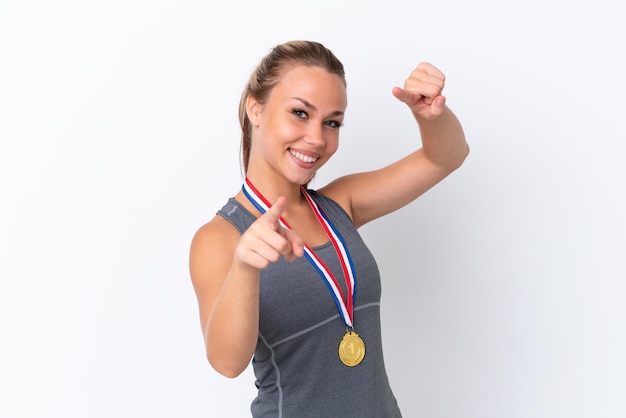 Junge sportliche Russin mit Medaillen isoliert auf weißem Hintergrund zeigt mit dem Finger auf Sie, während sie lächelt