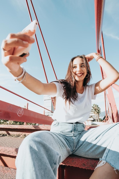 Junge städtische Mischlingsfrau, die ein Selfie macht, während sie an einem sonnigen Tag lächelt, urbaner Lebensstil, weiße T-Shirt-Leerstelle, trendiges soziales Netzwerk, junge Leute, Weitwinkelbild