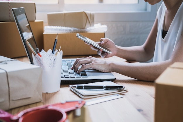 Junge starterunternehmerfrau, die zu hause mit intelligentem telefon arbeitet