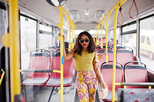 Junge stilvolle afroamerikanerfrau in der modernen sonnenbrille, die auf einem bus reitet.