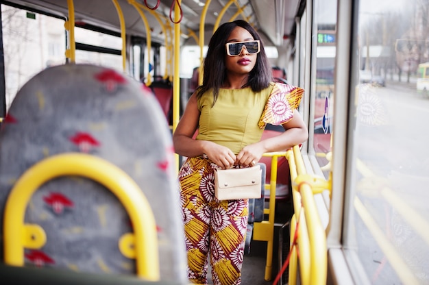 Junge stilvolle Afroamerikanerfrau in der modernen Sonnenbrille, die auf einem Bus reitet.