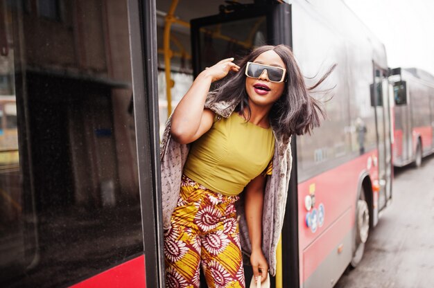 Junge stilvolle afroamerikanerfrau in der modernen sonnenbrille, die auf einem bus reitet.