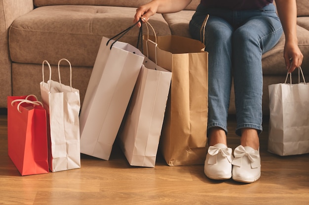 Junge stilvolle Frau, die Einkaufstaschen hält und auf einer Couch sitzt