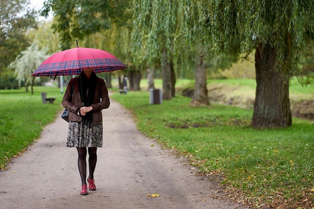 Foto junge, stilvolle frau, die mit einem riesigen roten regenschirm im herbstpark spazieren geht