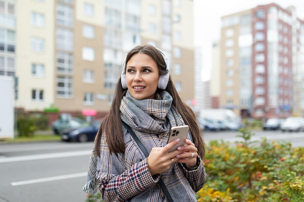 Junge stilvolle Frau, die mit Kopfhörern die Straße hinuntergeht und Musik vom Telefon hört