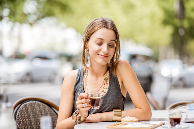 Junge stilvolle Frau im grauen Kleid trinkt Kaffee im Freien im Café in Paris