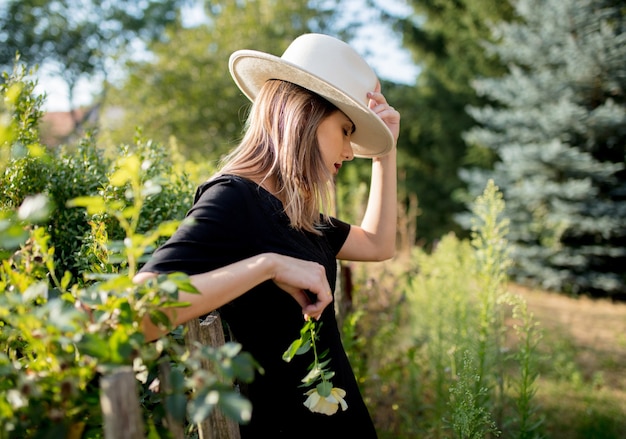 Junge stilvolle Frau im Hut in einem Garten der Sommerzeit