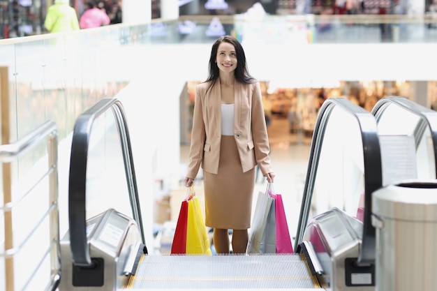 Junge stilvolle Frau klettert Rolltreppe mit Einkaufstüten im Einkaufszentrum