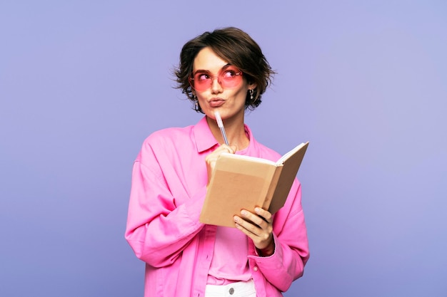 Junge, stilvolle Frau mit Sonnenbrille und einem ernsten Gesichtsausdruck hält einen Stift und ein Tagebuch