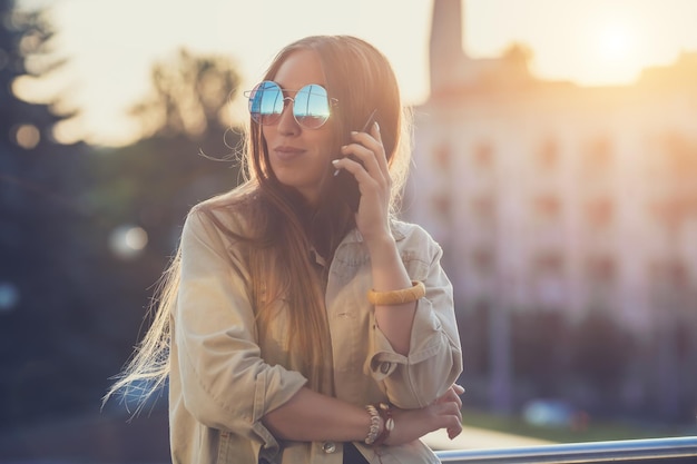 Junge stilvolle hübsche Frauenhände, die ein Telefon halten Sonnenunterganghintergrund Sonniger Tag Gutes Wetter Sonnenbrillen cooles Zubehör