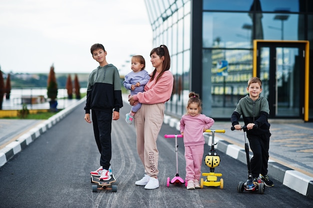 Junge stilvolle Mutter mit vier Kindern im Freien. Sportfamilie verbringen ihre Freizeit im Freien mit Rollern und Schlittschuhen.