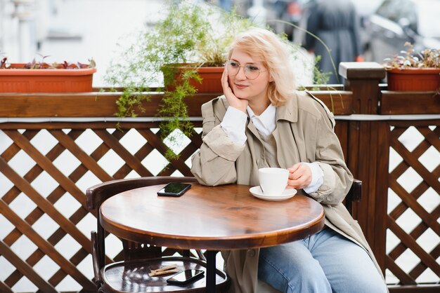 Junge stilvolle schöne Frau, die im Stadtcafé in der Straße sitzt