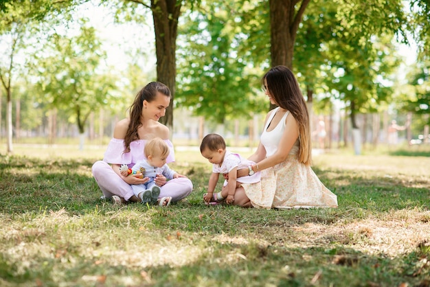 Junge stilvolle trendige Mütter sitzen mit ihren Töchtern im Gras in einem Park.