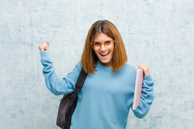 Junge Studentenfrau, die glücklich überrascht und stolz ist, Erfolg mit einem großen Lächeln schreiend und feiernd