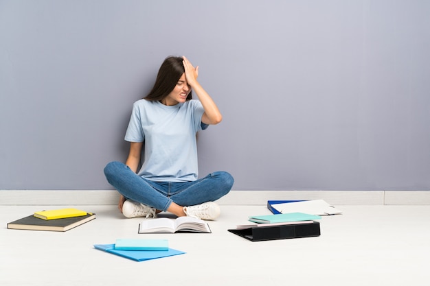 Junge studentenfrau mit vielen büchern auf dem boden, der zweifel hat und mit verwirren gesichtsausdruck