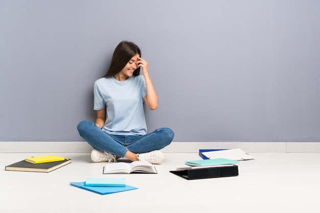 Junge Studentenfrau mit vielen Büchern auf dem Boden lachend