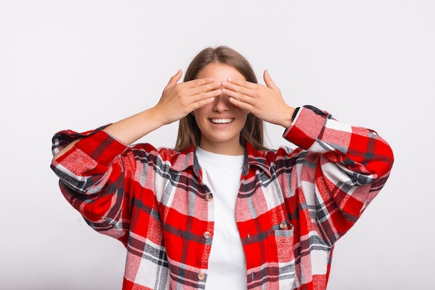 Junge Studentin bedeckt ihre Augen mit den Händen, während sie in die Kamera lächelt.