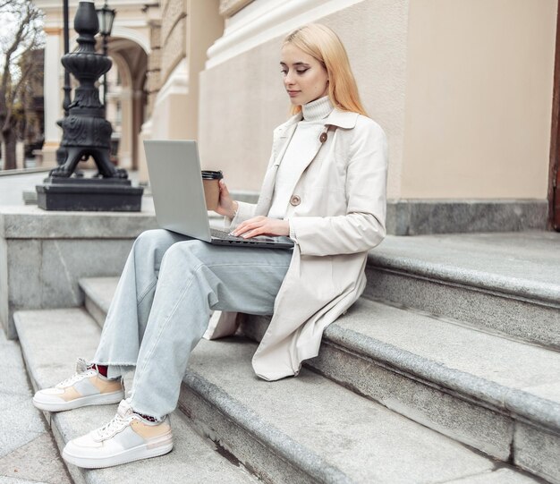 Junge Studentin benutzt Laptop, während sie in der Stadt auf einer Treppe sitzt