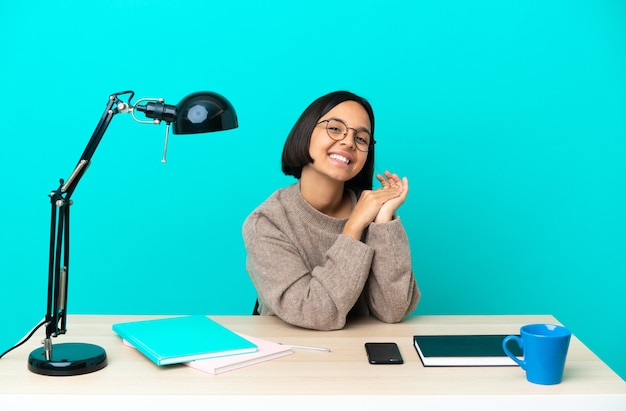 Junge Studentin der gemischten Rasse, die an einem applaudierenden Tisch studiert