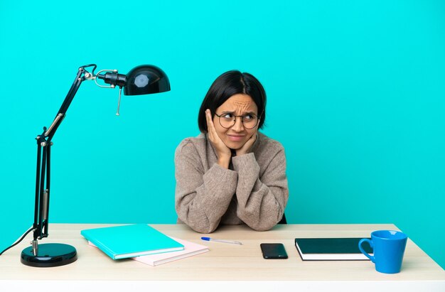 Junge Studentin der gemischten Rasse, die frustriert auf einem Tisch studiert und Ohren bedeckt