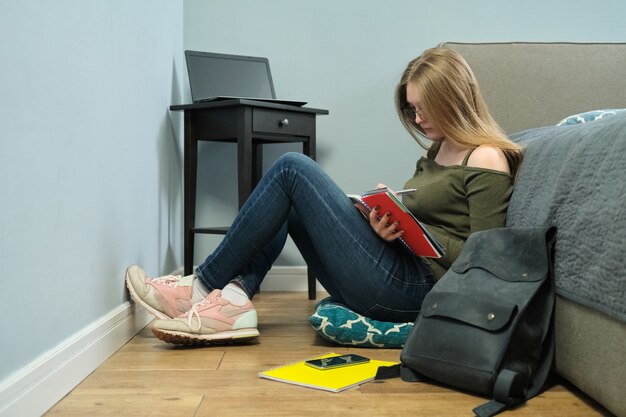 Junge Studentin der Universität mit Lehrbüchern, die zu Hause lesen und studieren, Fernunterricht. Kluges Mädchen mit Brille, die auf Boden sitzt