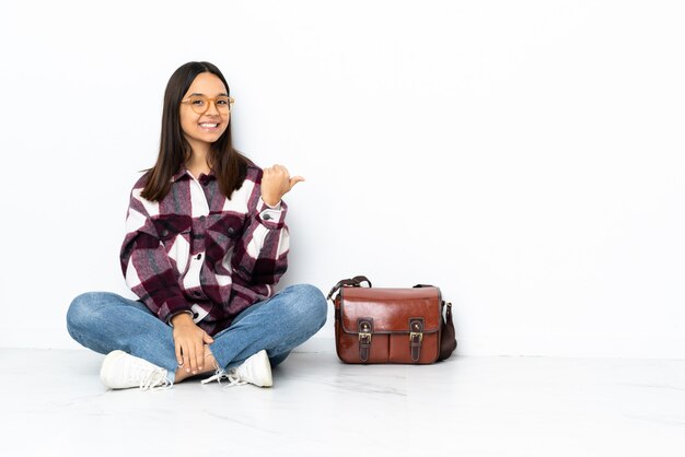 Junge Studentin, die auf dem Boden sitzt und zur Seite zeigt, um ein Produkt zu präsentieren